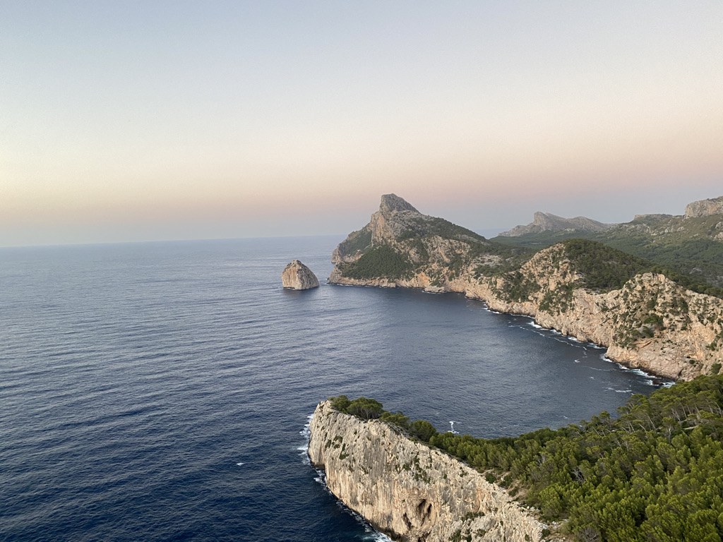 The Formentor peninsula at sunset, with cliffs dropping into a calm sea and a rock islet offshore