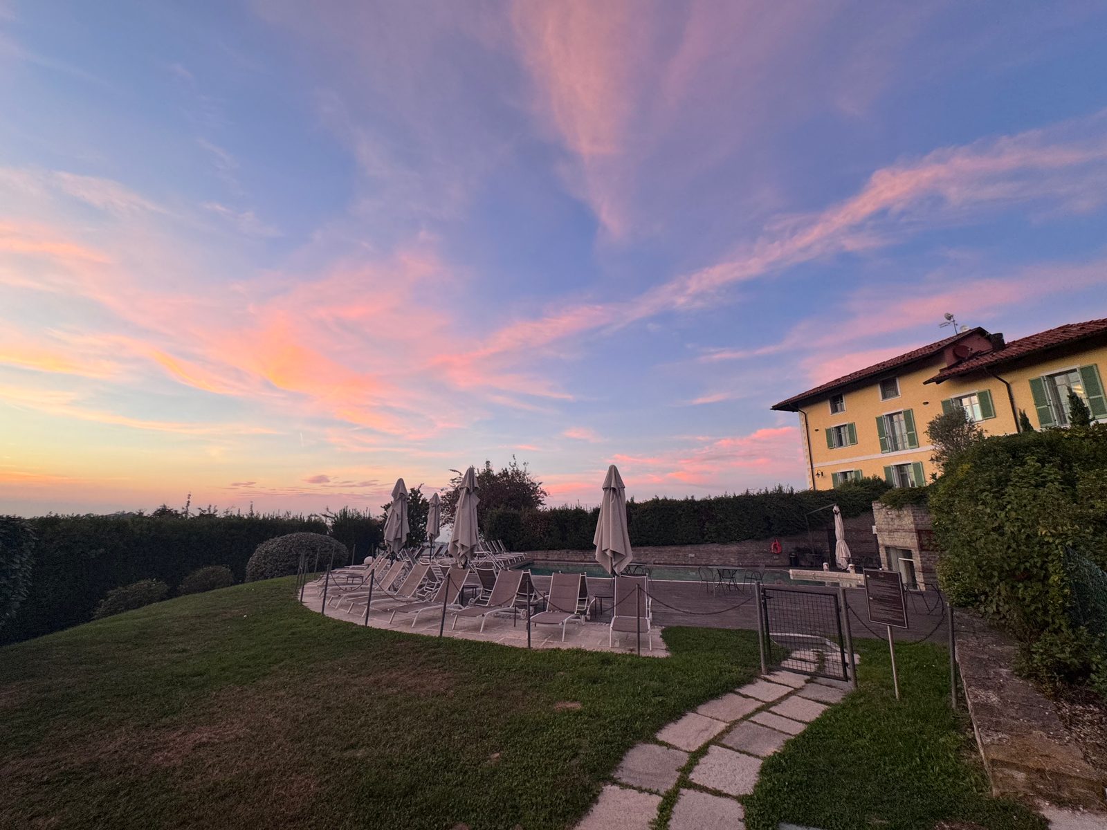 Sunset over the pool terrace at Villa d'Amelia, with closed umbrellas, loungers and the yellow house on the right