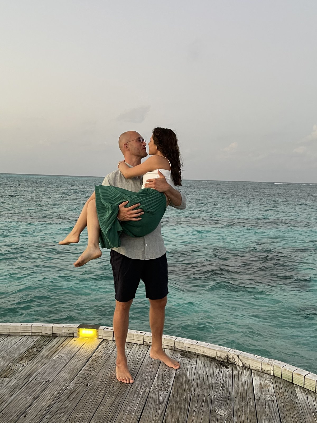 Thomas carrying Teri at the edge of a wooden deck over the lagoon at Six Senses Laamu